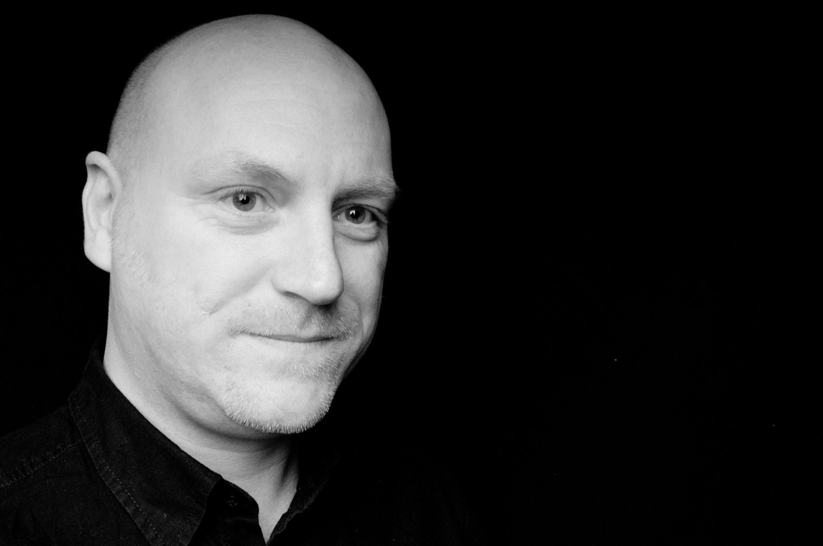 Black and white studio portrait of Elliott Richmond against a black background, looking at the camera